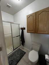 Master bathroom featuring a textured ceiling, a shower stall, and light tile patterned flooring