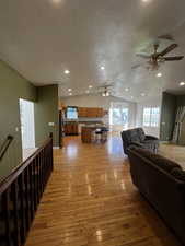 Living area with light wood finished floors, lofted ceiling, a textured ceiling, a ceiling fan, and recessed lighting