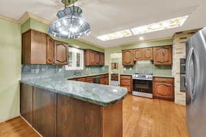 Kitchen featuring brown cabinets, decorative backsplash, dark stone countertops, a peninsula, and crown molding