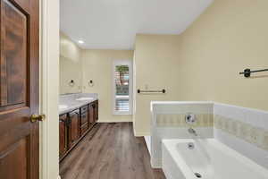 Bathroom featuring double vanity, a garden tub, dark wood-type flooring, and recessed lighting