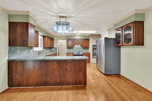 Kitchen with appliances with stainless steel finishes, a peninsula, backsplash, light wood finished floors, and dark stone counters