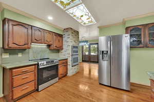 Kitchen featuring ornamental molding, stainless steel appliances, backsplash, light wood-style flooring, and brown cabinets