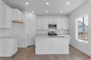 Kitchen featuring recessed lighting, white cabinetry, appliances with stainless steel finishes, an island with sink, and light wood-style flooring