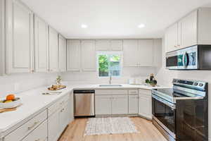 Kitchen with appliances with stainless steel finishes, light wood-type flooring, recessed lighting, light countertops, and white cabinets