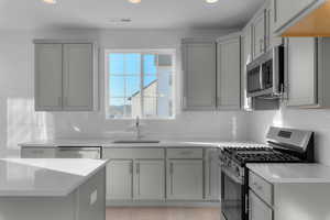 Kitchen featuring appliances with stainless steel finishes, gray cabinetry, light stone counters, and recessed lighting
