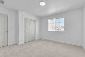 Unfurnished bedroom with a textured ceiling, light colored carpet, and a closet