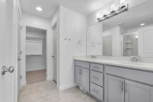 Full bathroom with double vanity, a stall shower, a spacious closet, a textured ceiling, and light carpet