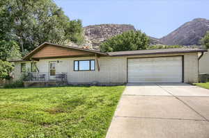 Ranch-style house with a garage, brick siding, concrete driveway, a front yard, and a mountain view