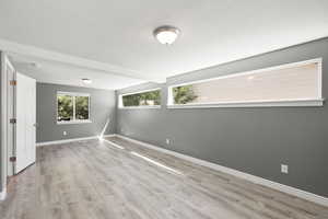 Empty room with light wood-style floors, a textured ceiling, and beam ceiling