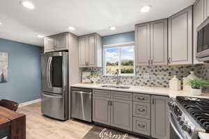 Kitchen with gray cabinets, appliances with stainless steel finishes, light wood-style flooring, backsplash, and light stone countertops