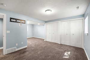 Unfurnished bedroom with dark carpet, multiple closets, and a textured ceiling