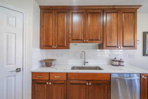 Kitchen featuring tasteful backsplash, dishwasher, light quartz countertops, and brown cabinets