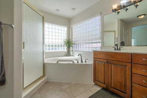 Primary Bathroom featuring light tile patterned floors, a shower stall, vanity, and a bath