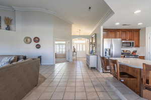 Kitchen featuring ornamental molding, brown cabinetry, light tile patterned flooring, appliances with stainless steel finishes, and tasteful backsplash