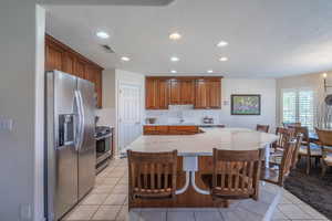 Kitchen with a textured ceiling, stainless steel appliances, decorative backsplash, quartz counters, light tile patterned floors, and a breakfast bar area with suspended seating