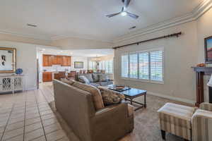 Carpeted living area featuring a chandelier, light tile patterned floors in walking areas, a ceiling fan, ornamental molding, and a tile fireplace
