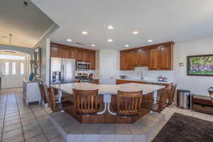 Kitchen with light tile patterned floors, a kitchen breakfast bar with suspended seating, decorative backsplash, stainless steel appliances, and a textured ceiling