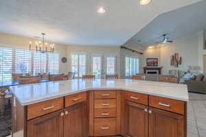 Kitchen with brown cabinetry, quartz counters, a textured ceiling, open floor plan, a ceiling fan, and a fireplace