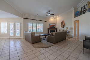 Living room with light carpet just beyond tile patterned flooring, crown molding, arched walkways, a ceiling fan, and a fireplace