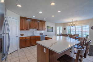 Kitchen with stainless steel appliances, light tile patterned floors, tasteful backsplash, brown cabinetry, and a textured ceiling