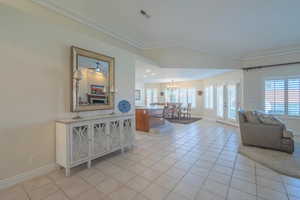 Great room with light tile patterned floors, vaulted ceiling, a chandelier, and crown molding
