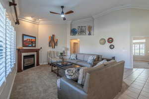 Carpeted living area with ornamental molding, a fireplace, a ceiling fan, a towering ceiling, and tile patterned floors