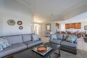 Carpeted living area with light tile patterned floors in the walkway and kitchen, ornamental molding, arched walkways, and recessed lighting