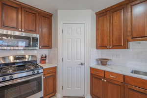 Kitchen with stainless steel appliances, tasteful backsplash, light quartz counters, brown cabinets, and a textured ceiling