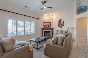 Carpeted living room with a ceiling fan, crown molding, a fireplace, light tile patterned floors in the walkway, and arched walkways