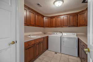 Laundry room featuring a textured ceiling, light tile patterned flooring, cabinet space, and washing machine and dryer