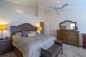 Carpeted primary bedroom featuring crown molding, ceiling fan, and a towering ceiling