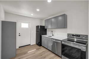 Kitchen with gray cabinets, appliances with stainless steel finishes, light wood-type flooring, recessed lighting, and light stone counters