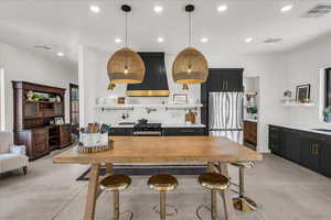 Kitchen with freestanding refrigerator, custom range hood, finished concrete floors, recessed lighting, and dark cabinetry