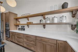 Kitchen featuring open shelves, stainless steel appliances, decorative light fixtures, brown cabinetry, and finished concrete floors