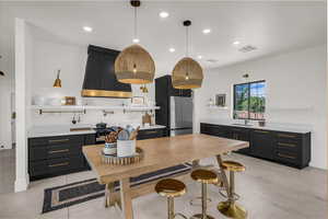 Kitchen featuring dark cabinetry, premium range hood, open shelves, recessed lighting, and freestanding refrigerator