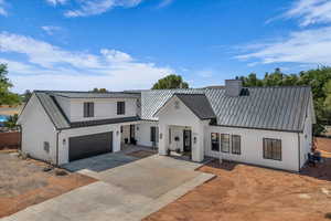 Modern farmhouse with a garage, a metal roof, concrete driveway, and stucco siding