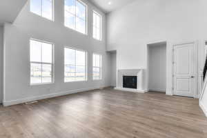 Unfurnished living room with a glass covered fireplace, a high ceiling, and light wood-style floors