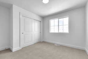 Unfurnished bedroom with light carpet, a textured ceiling, and a closet
