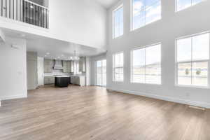 Unfurnished living room with healthy amount of natural light, light wood-style floors, a towering ceiling, and a chandelier