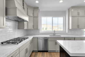 Kitchen featuring appliances with stainless steel finishes, premium range hood, light stone countertops, recessed lighting, and light wood-style flooring