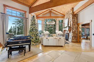 Living area with a chandelier, plenty of natural light, light wood finished floors, high vaulted ceiling, and a wood ceiling with exposed beams