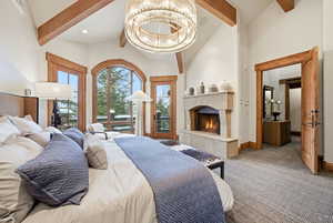 Carpeted bedroom with access to exterior, a tiled fireplace, beamed ceiling, a chandelier, and high vaulted ceiling
