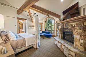 Bedroom featuring a fireplace, beam ceiling, dark colored carpet, connected bathroom, and access to outside