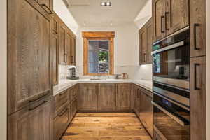 Kitchen featuring light wood-style flooring, appliances with stainless steel finishes, brown cabinetry, and light stone countertops