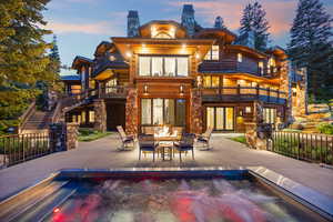 Back of house with a chimney, a patio, a balcony, stone siding, and an outdoor living space with a fire pit