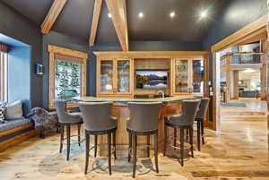 Bar area with glass insert cabinets, light wood-style flooring, light countertops, recessed lighting, and beamed ceiling