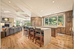 Kitchen featuring brown cabinetry, a kitchen breakfast bar, beam ceiling, light stone counters, and a stone fireplace
