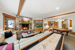 Living area featuring arched walkways, a stone fireplace, billiards, beamed ceiling, and stairs