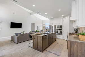 Kitchen with a breakfast bar, appliances with stainless steel finishes, decorative backsplash, a kitchen island with sink, and high vaulted ceiling