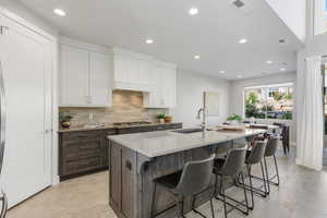 Kitchen featuring backsplash, white cabinets, an island with sink, recessed lighting, and dark brown cabinets